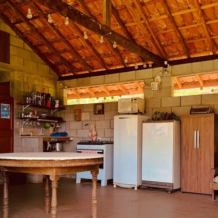 Área com geladeira, freezer, fogão, pia, louças e uma mesa. Tudo muito bem iluminado